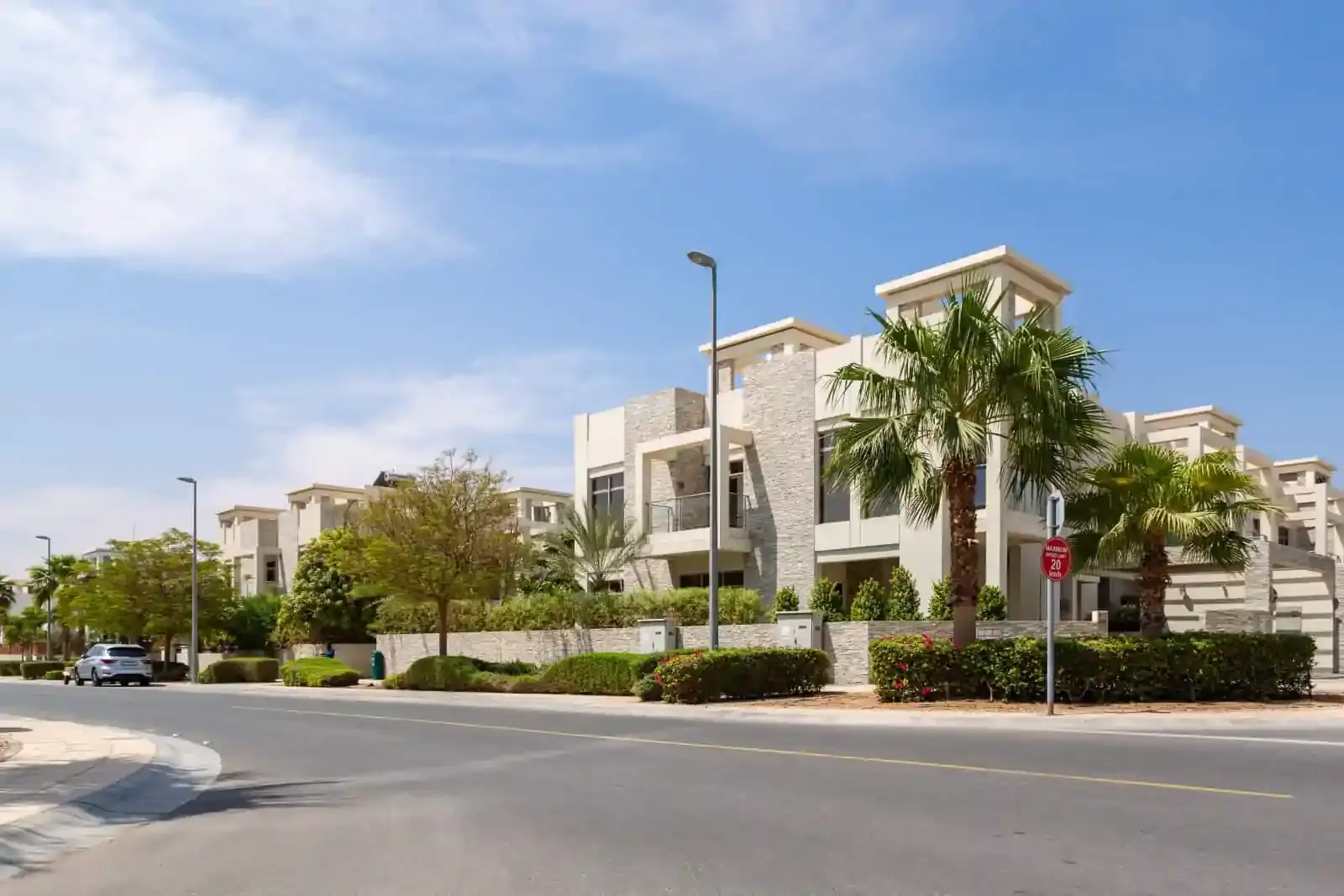 Modern white stone townhouses with palm trees and a clean road under a blue sky.